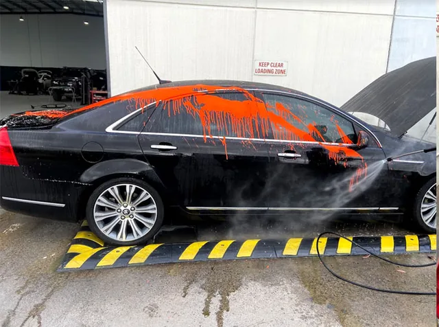 Black sedan covered in orange paint overspray before removal