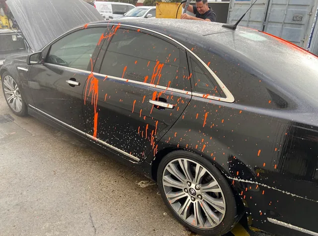 Orange overspray down the side of a black sedan before treatment